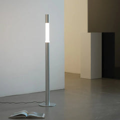 Modern cylindrical floor lamp with silver finish in minimalistic room, book on floor