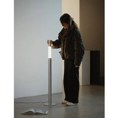 Woman standing beside a modern LED floor lamp in a minimalist room with an open book on the floor.