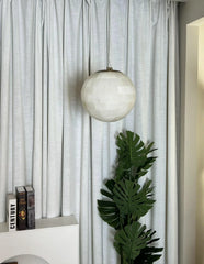 Modern alabaster ball pendant light hanging in a room with white curtains and green plant
