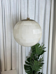 Modern alabaster ball pendant light with brass accents hanging in front of white curtains and green leaves