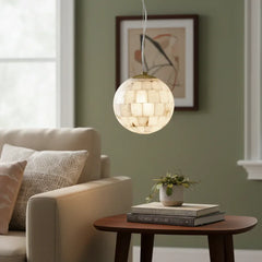 Alabaster ball pendant light hanging above a wooden side table with books and a small plant in a cozy living room