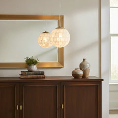 Modern alabaster ball pendant light hanging above dark wood sideboard with mirror, books, and pottery