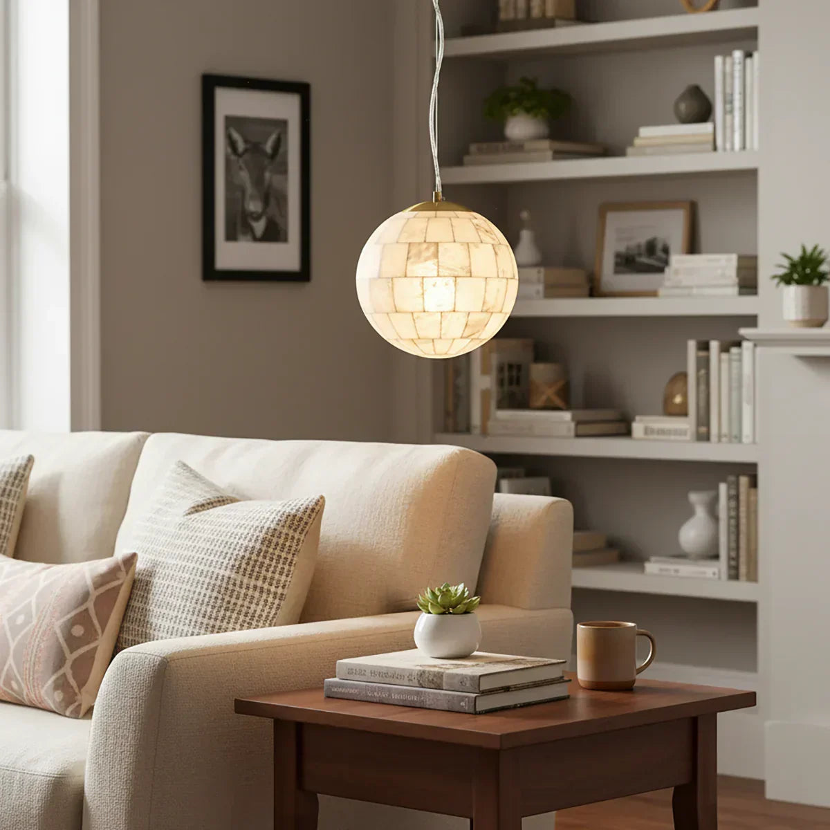 Alabaster ball pendant light hanging above beige sofa and wooden side table with books and mug in cozy living room