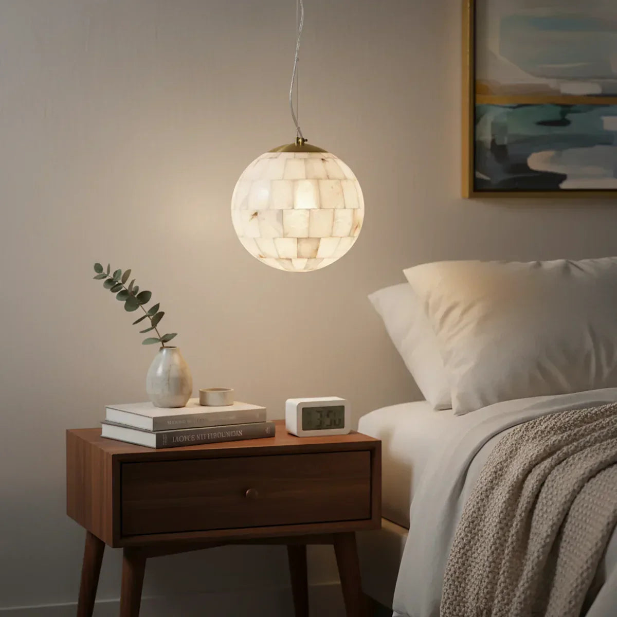 Alabaster ball pendant light hanging above a wooden bedside table with books, vase, and alarm clock in a modern bedroom
