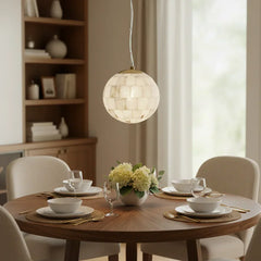 Modern alabaster ball pendant light hanging above a wooden dining table set with white dinnerware and floral centerpiece