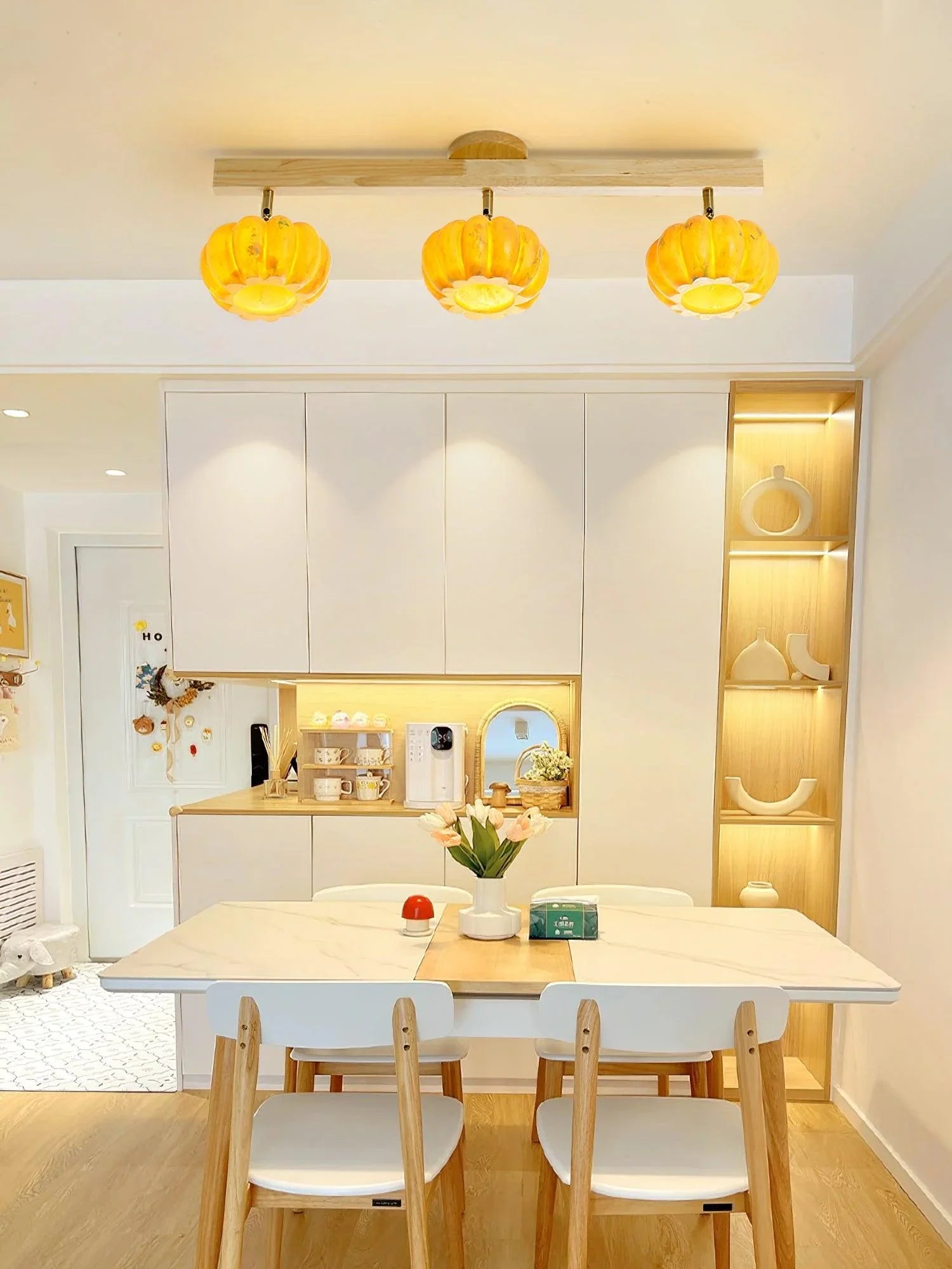 Modern kitchen with pumpkin-shaped yellow ceiling lamps, wood dining set, and white cabinets