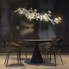 Modern gold and white gingko leaf chandelier hanging above a round black dining table with four contemporary chairs in a minimalist room