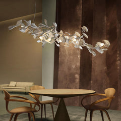 Modern gold and white Gingko leaf chandelier above round wooden dining table with four wooden chairs in stylish room