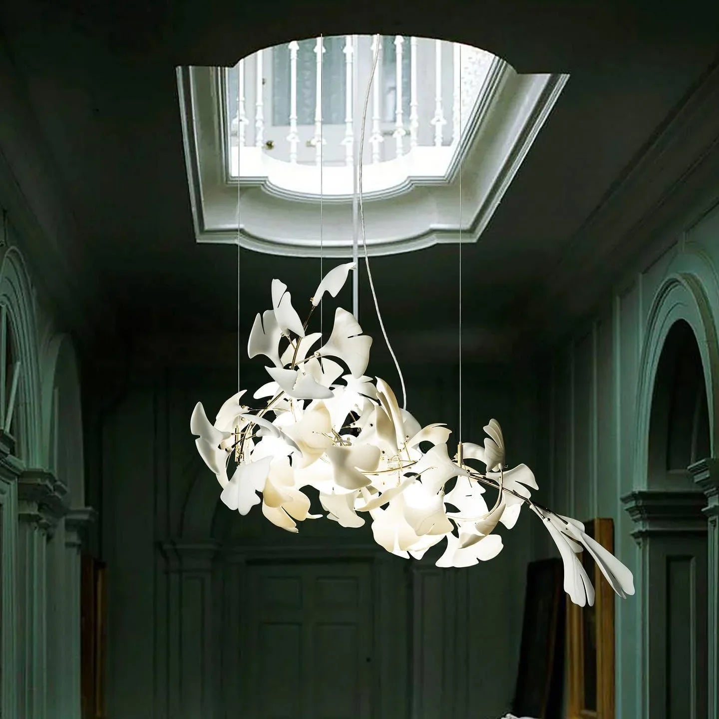 Modern gold and white ginkgo leaf chandelier hanging in elegant hallway with skylight