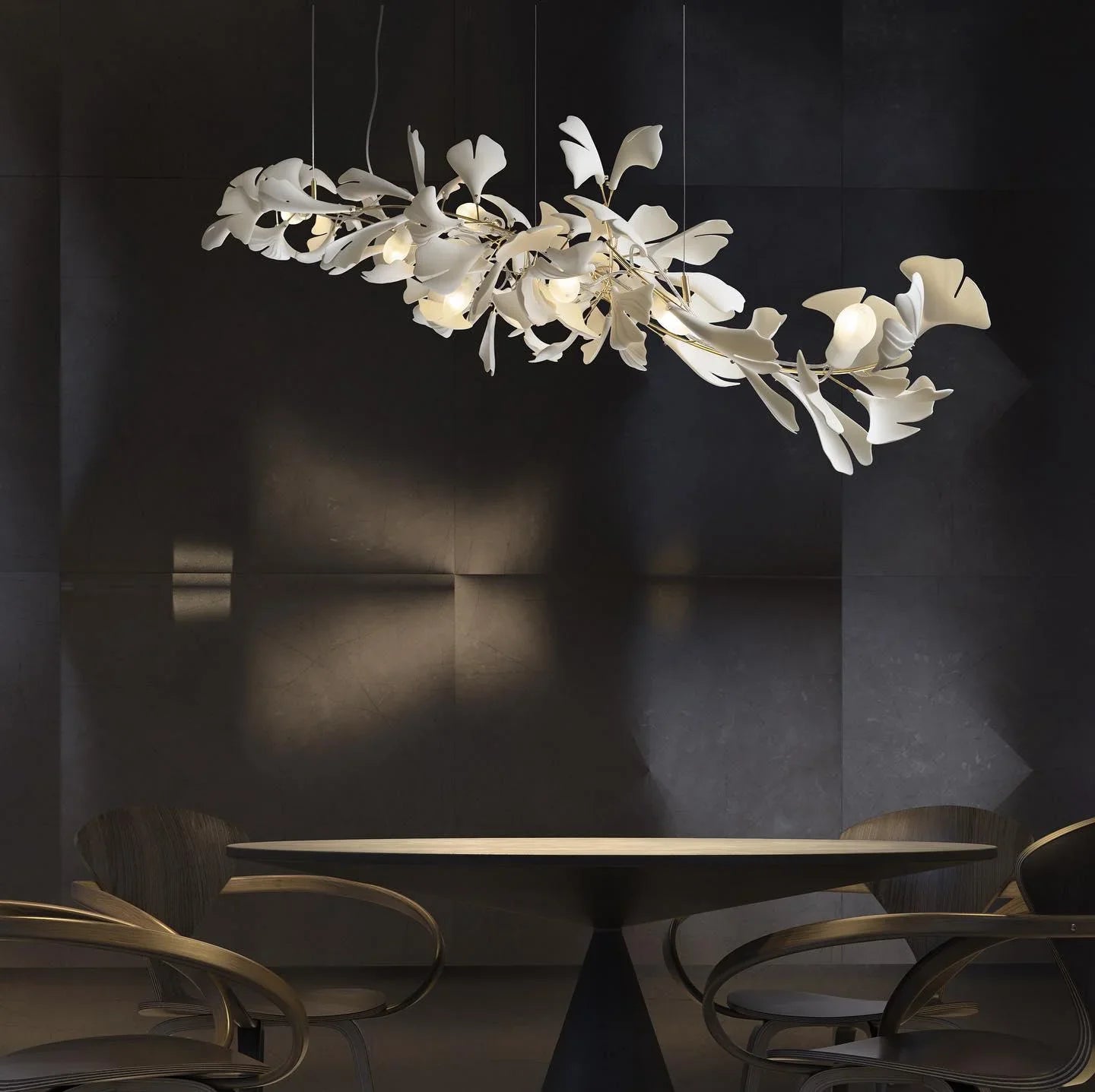 Modern ginkgo leaf chandelier with gold accents hanging above a round dining table in a dark, minimalist room