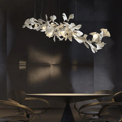 Modern ginkgo leaf chandelier with gold accents hanging above a round dining table in a dark, minimalist room