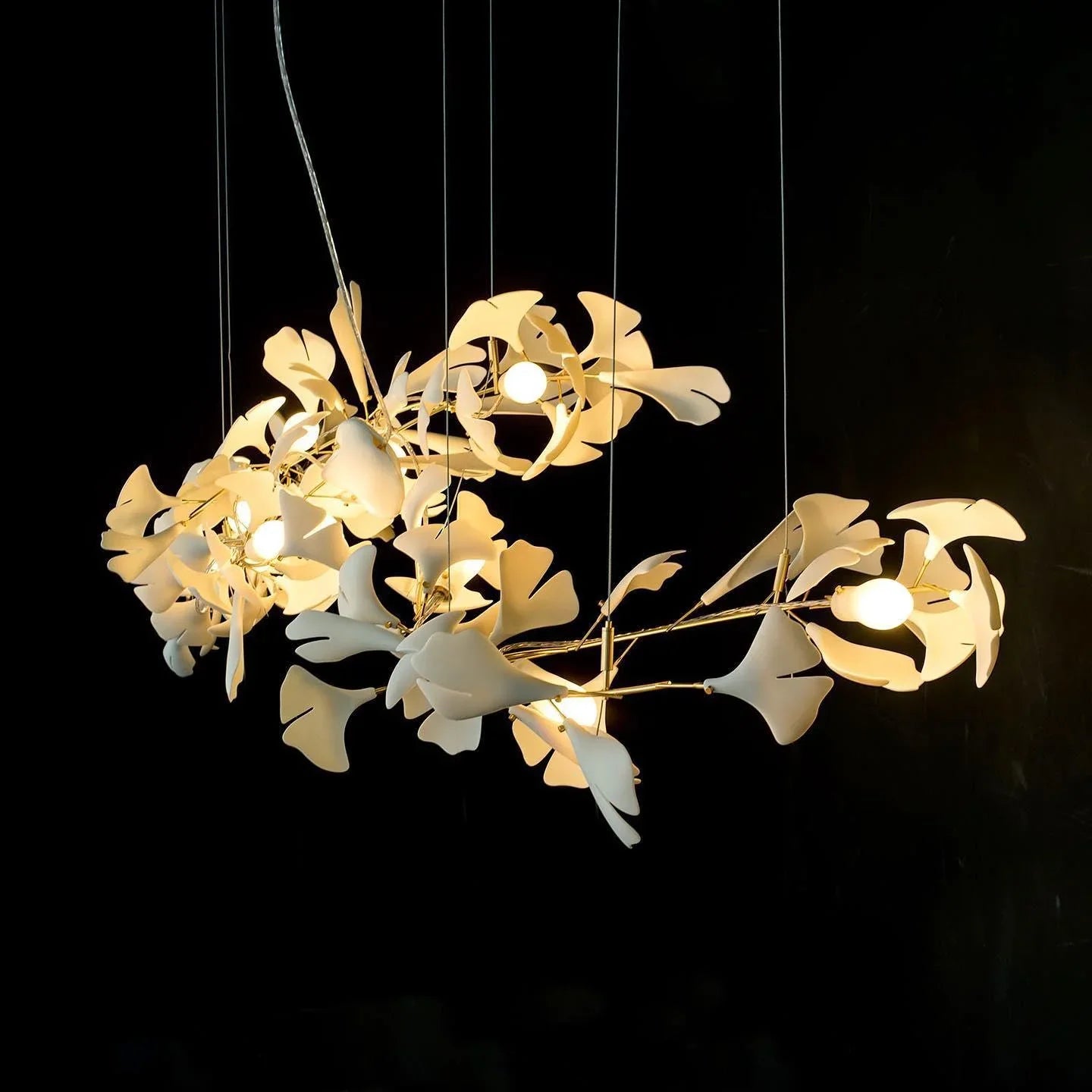 Modern gold and white ginkgo leaf chandelier with multiple light bulbs hanging on black background