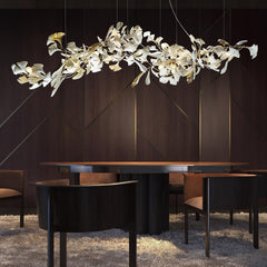 Modern gold and white Gingko leaf chandelier over round dining table in elegant dark wood interior