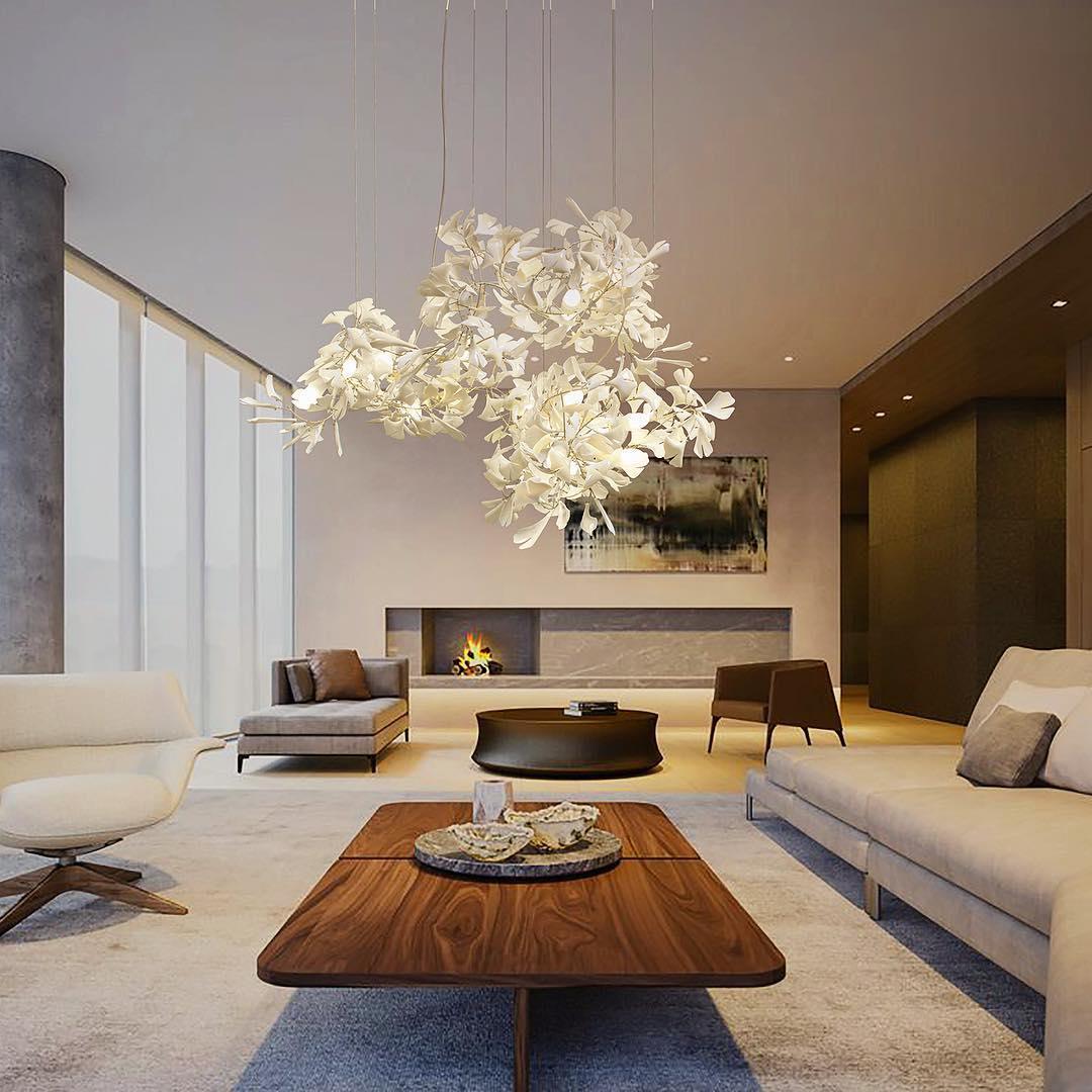 Modern living room featuring a white and gold gingko leaf chandelier above a wooden coffee table with stone decor.