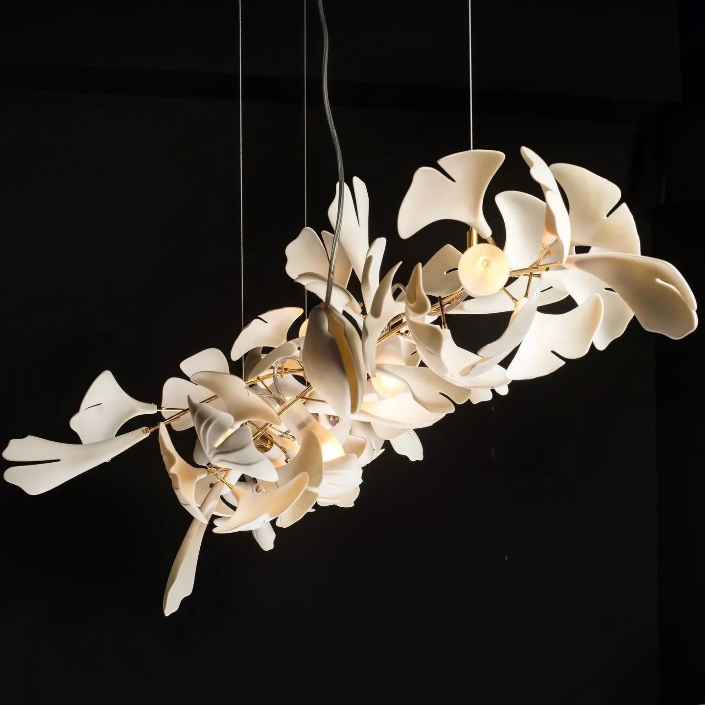 Modern gold and white Gingko leaf chandelier with multiple lights suspended against a black background