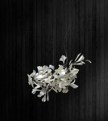 Modern white gingko leaf chandelier with gold accents hanging against dark wood wall