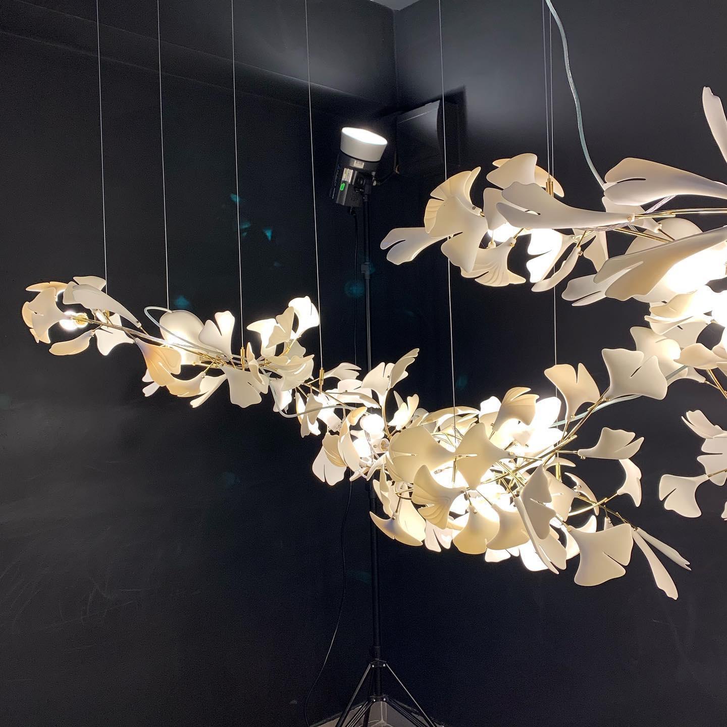 Modern gold and white Gingko leaf chandelier with multiple illuminated branches against a dark background