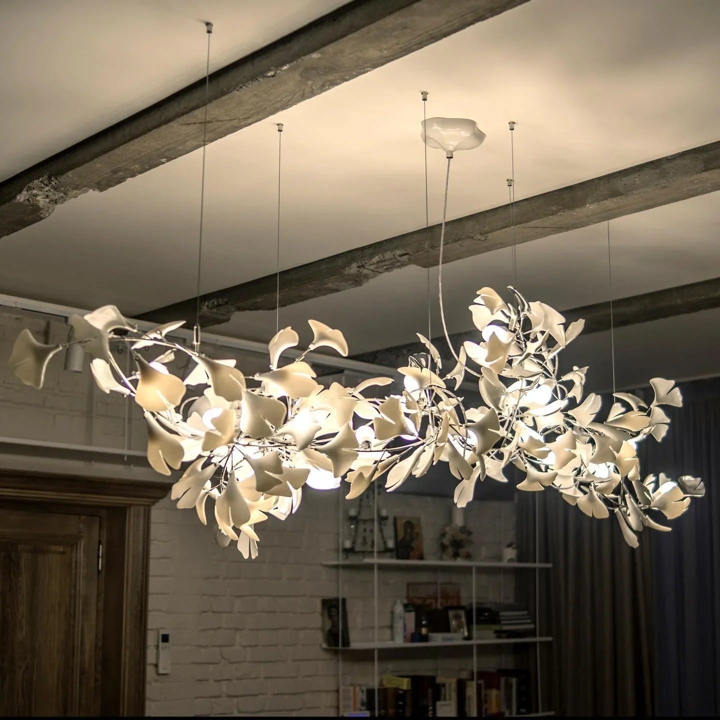 Modern gold and white gingko leaf chandelier suspended from a ceiling with exposed beams in a cozy room