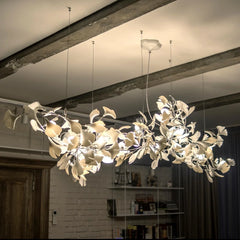 Modern gold and white gingko leaf chandelier suspended from a ceiling with exposed beams in a cozy room