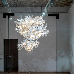 Modern white ginkgo leaf chandelier with gold branches hanging in gallery space with wooden beam ceiling