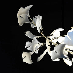 Modern gold and white ginkgo leaf chandelier with sculptural design, illuminated against black background