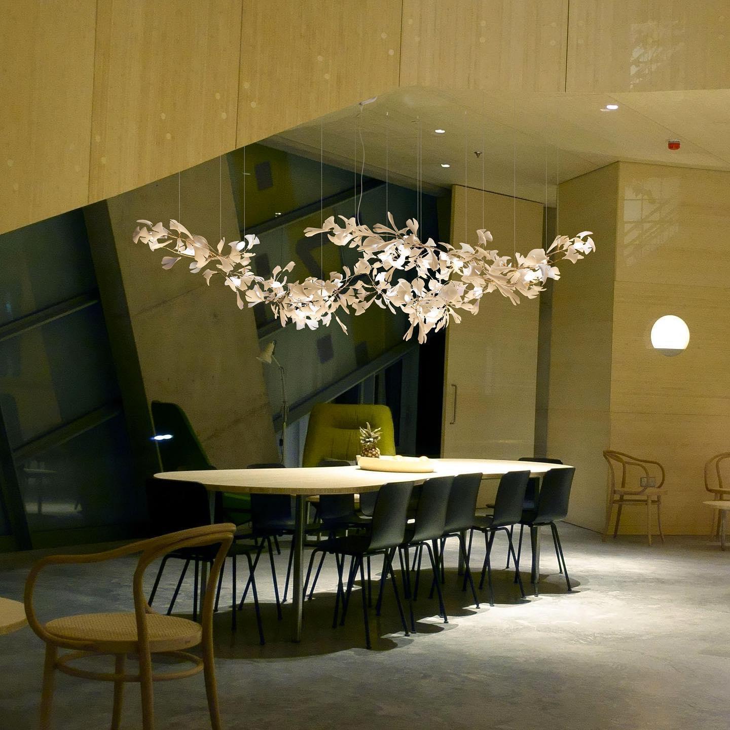 Modern white gingko leaf chandelier above long dining table with black chairs in stylish room