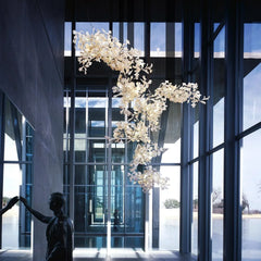 Modern gold and white gingko leaf chandelier in high-ceilinged glass room with reflective sculpture
