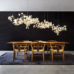 Modern gold and white Gingko leaf chandelier above wooden dining table with six chairs on dark rug