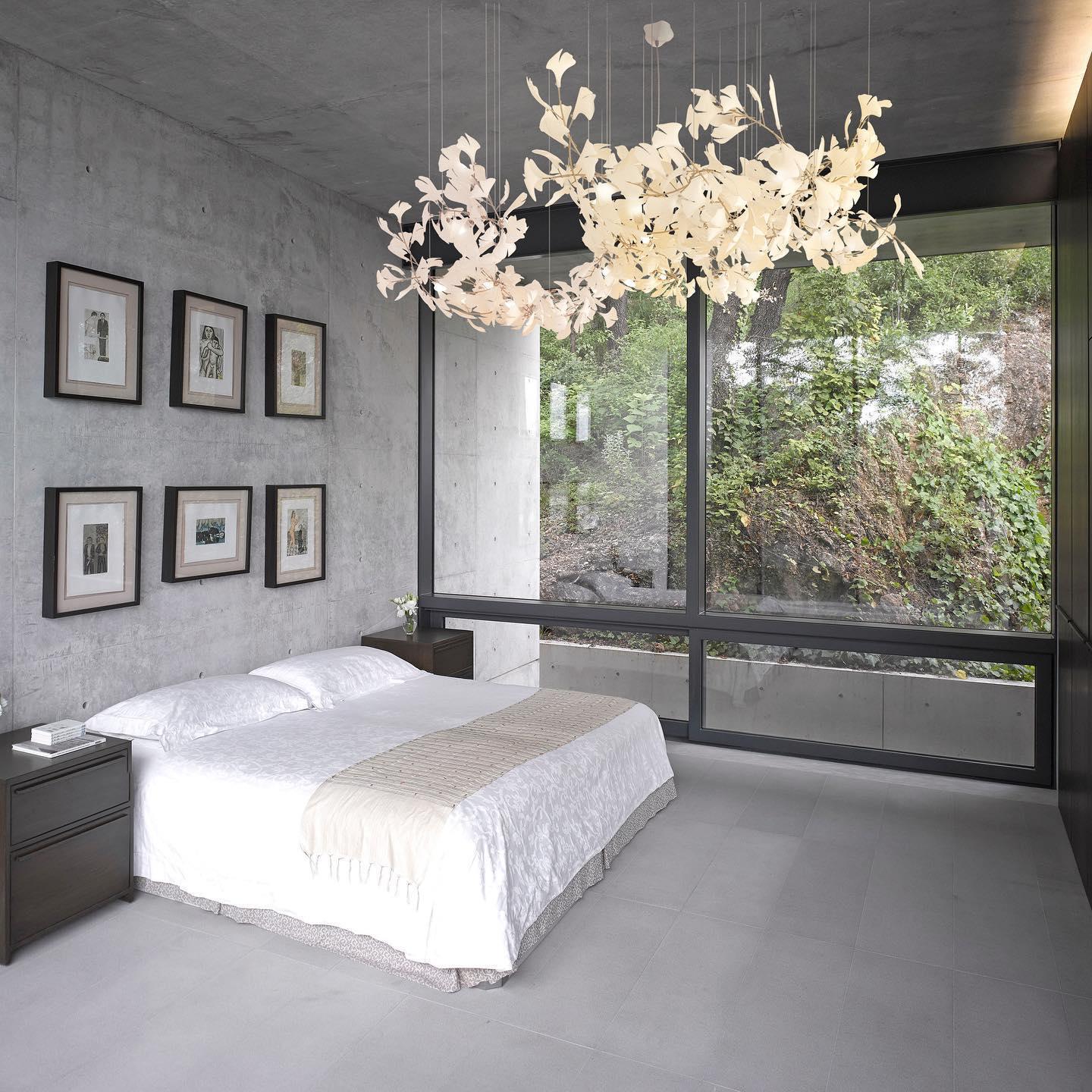 Modern bedroom with concrete walls, large window, dark wood nightstands, and white gold gingko chandelier