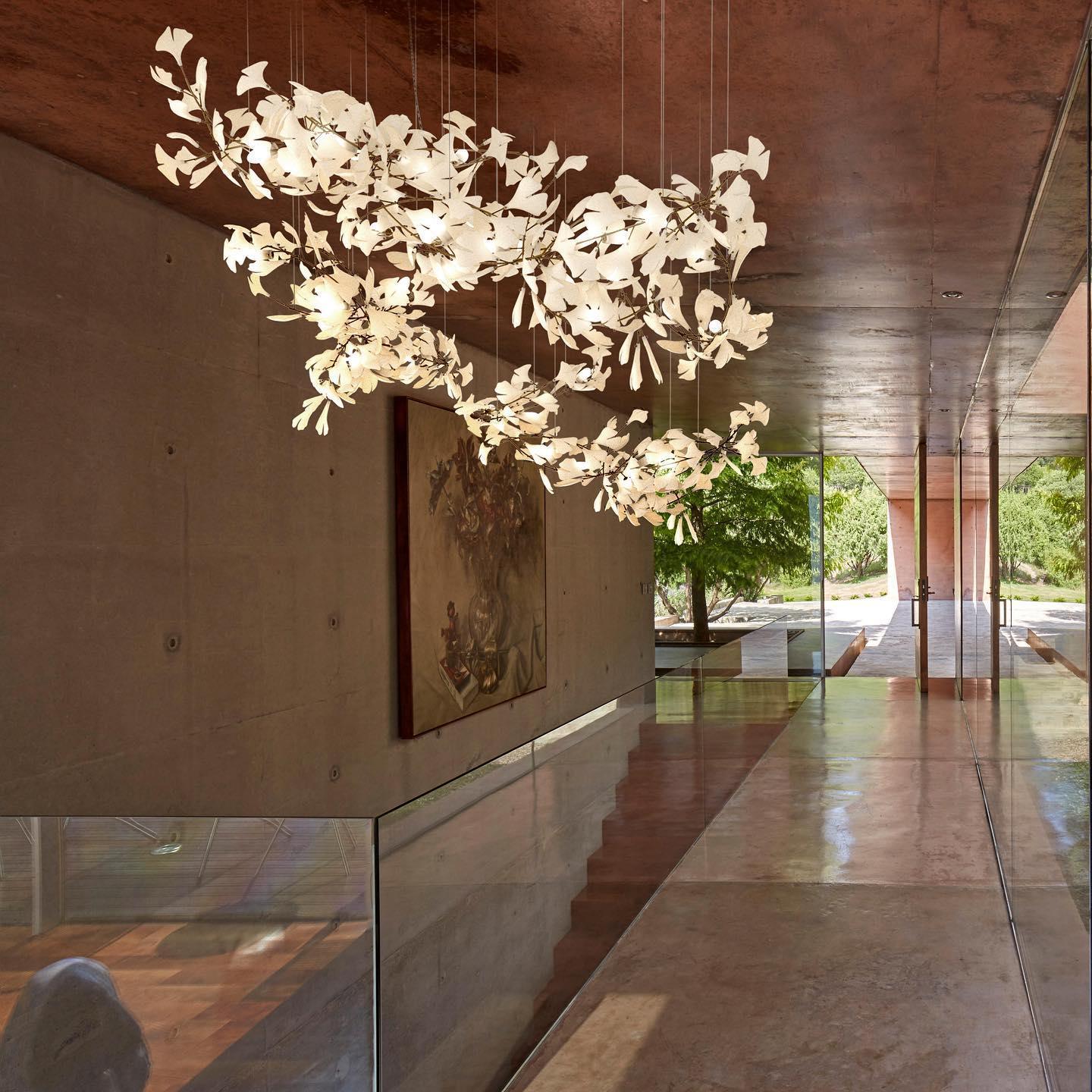 Modern gold and white gingko leaf chandelier hanging in a minimalist concrete and glass hallway