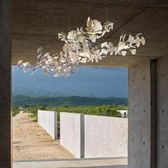 Modern gold and white gingko leaf chandelier suspended in a concrete room with outdoor nature view