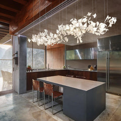 Modern kitchen with large gray island, brown woven chairs, stainless steel appliances, and white gingko leaf chandelier