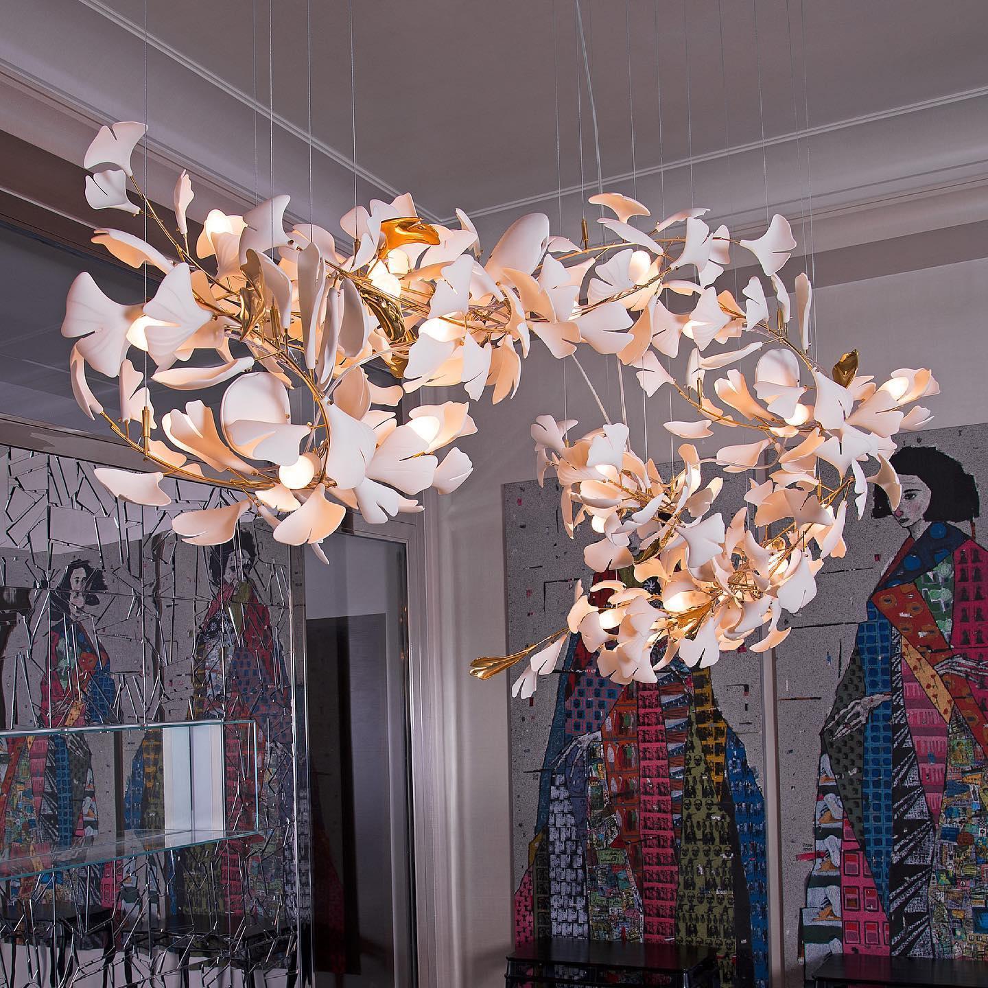 Modern gold and white ginkgo leaf chandelier hanging in contemporary room with colorful abstract wall art