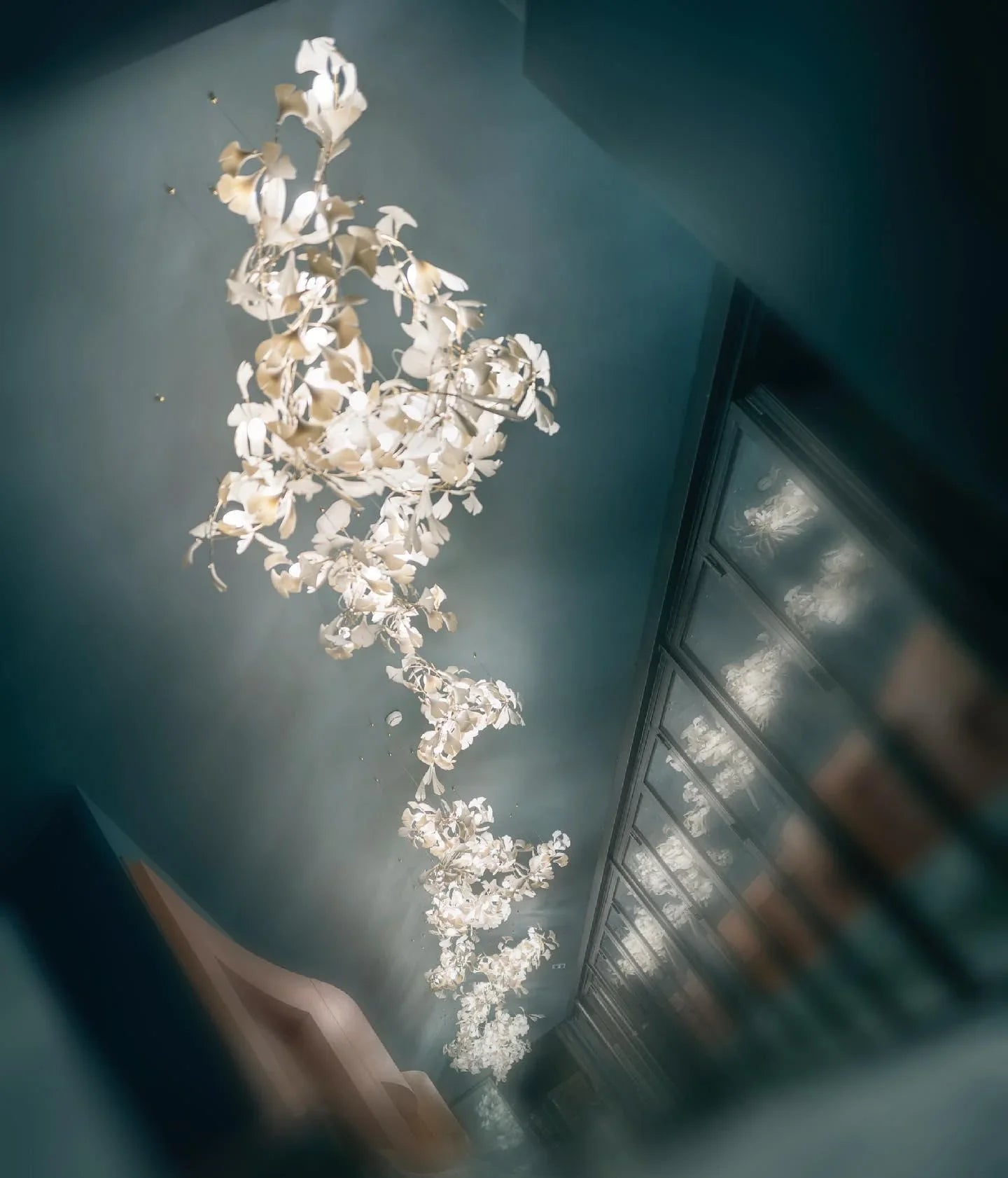 YH Lamps modern gold and white ginkgo leaf chandelier hanging on ceiling with reflections on glass wall