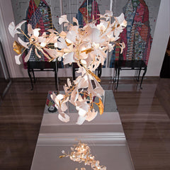 Modern gold and white gingko leaf chandelier hanging above reflective surface in stylish room with colorful wall art