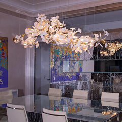 Modern gold and white gingko leaf chandelier above glass dining table with beige chairs in stylish room