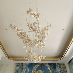 Modern gold and white gingko leaf chandelier hanging from ceiling in elegant room with blue marble wall art