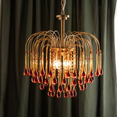 Elegant brass chandelier with amber glass teardrop pendants hanging, warm light glowing in front of dark curtains