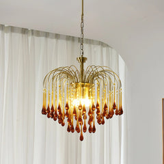 Modern brass chandelier pendant lamp with amber glass teardrop accents hanging in a bright room with white curtains