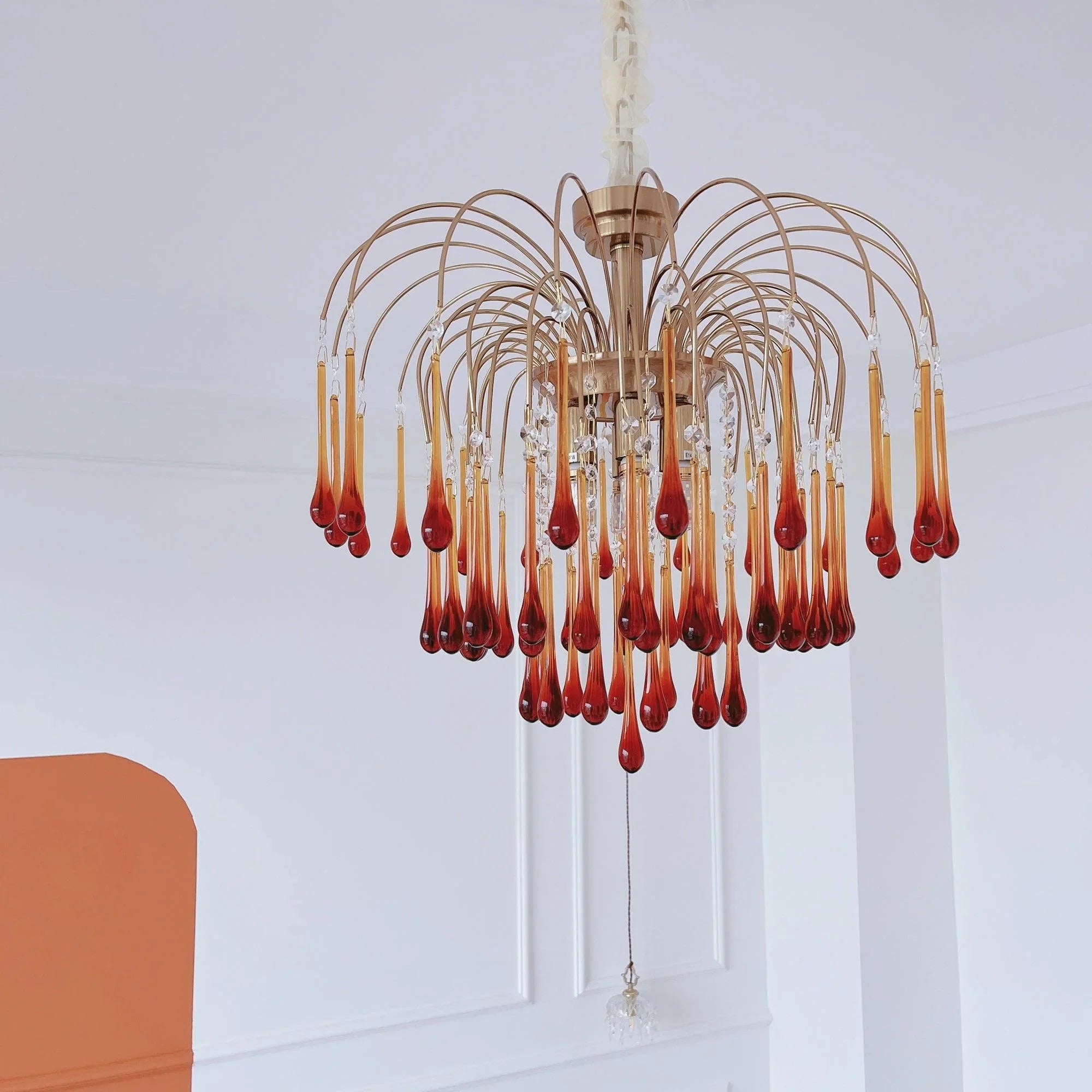 Modern brass chandelier with amber teardrop glass pendants hanging in a minimalist white room