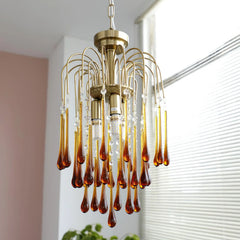 Modern brass chandelier pendant lamp with amber glass teardrop accents hanging near window blinds