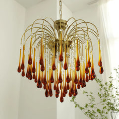 Modern brass chandelier with amber glass teardrop pendants hanging in bright room with white walls and green plant