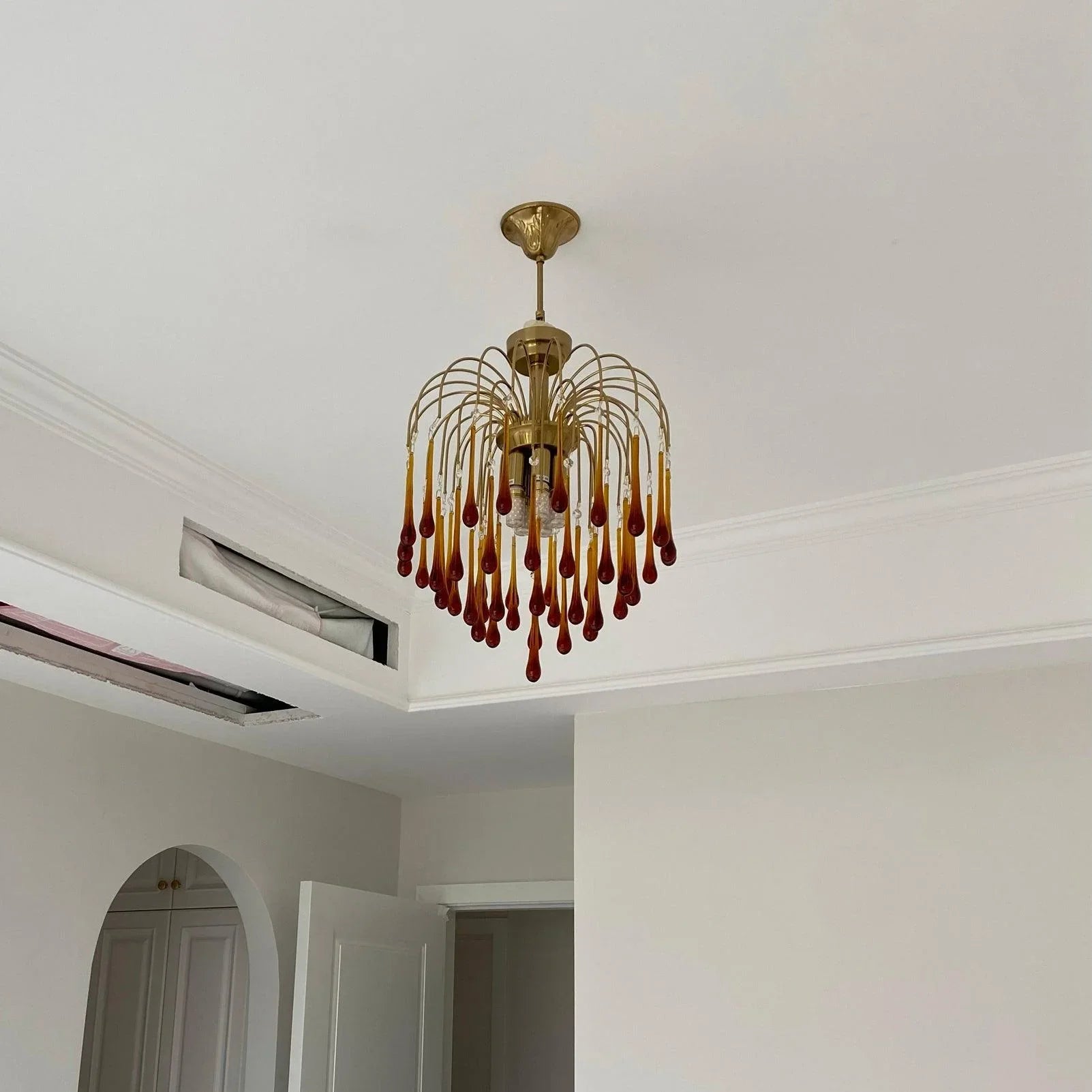 Modern brass chandelier pendant lamp with amber glass teardrop accents hanging from white ceiling