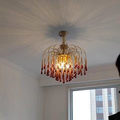 Modern brass chandelier pendant lamp with amber glass teardrops casting shadows on ceiling in living room