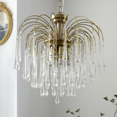 Modern brass chandelier pendant lamp with multiple clear glass teardrop crystals hanging in a bright room