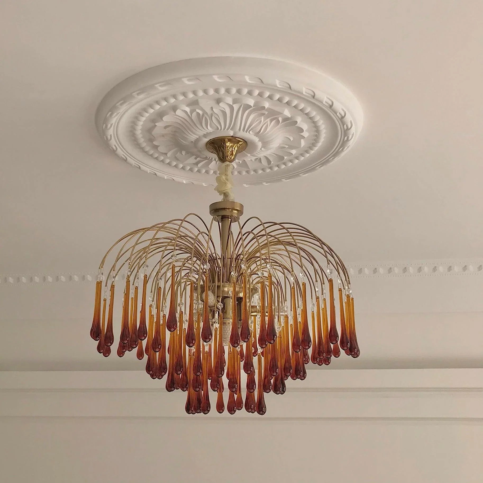 Modern brass chandelier with amber glass teardrop pendants hanging from decorative white ceiling medallion