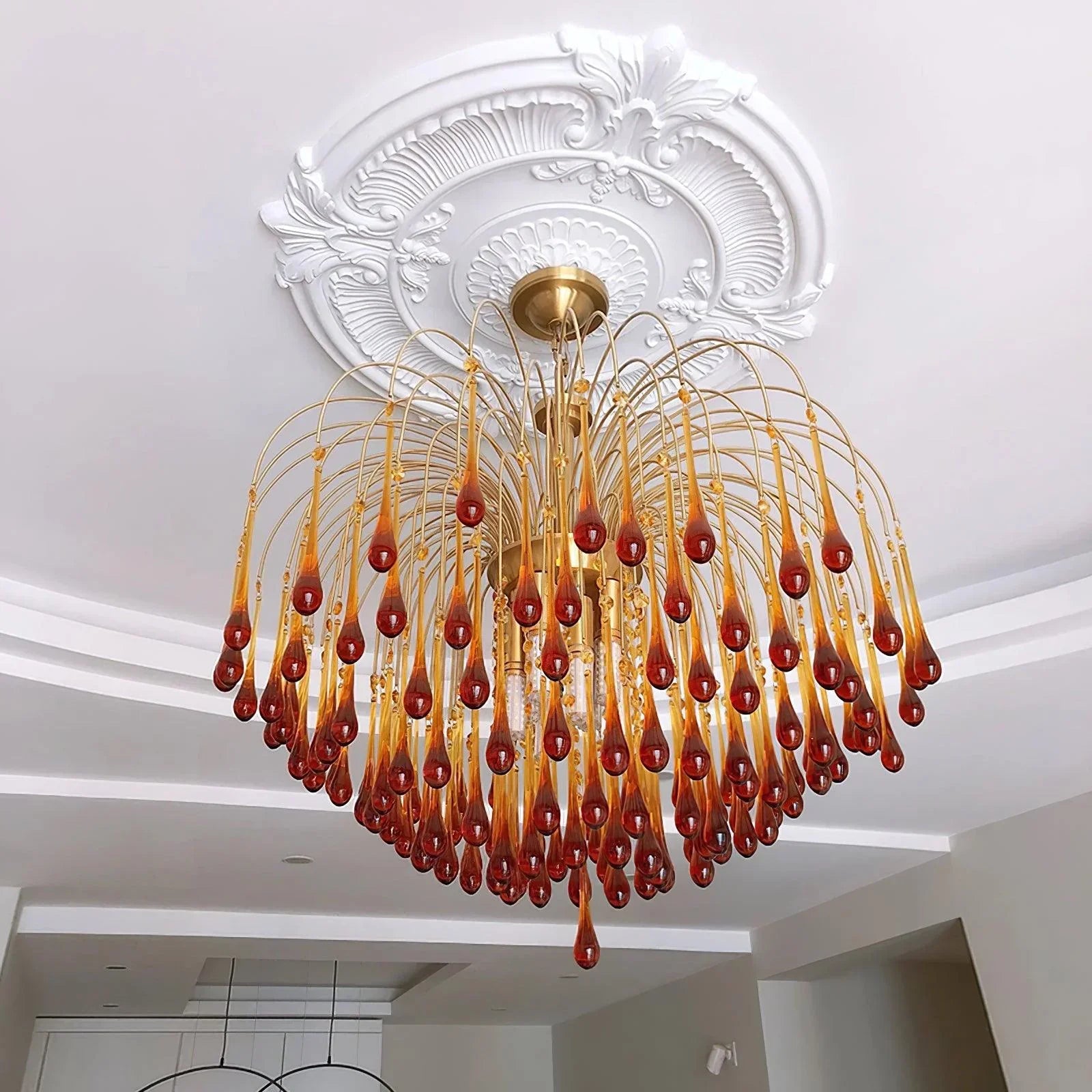 Modern brass chandelier with amber glass droplets hanging from ceiling medallion in elegant living space