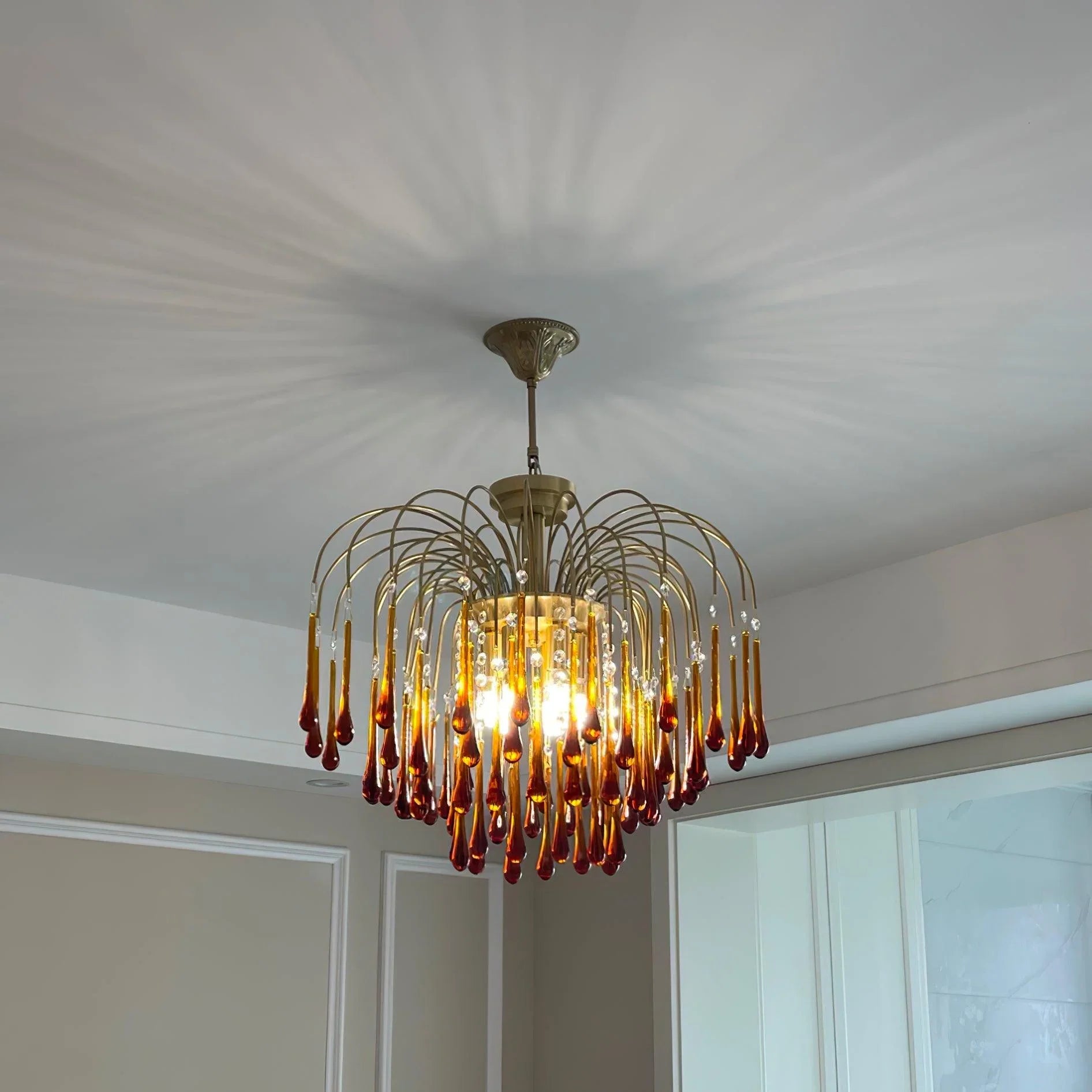 Modern brass chandelier with amber glass droplet accents hanging from ceiling in elegant room