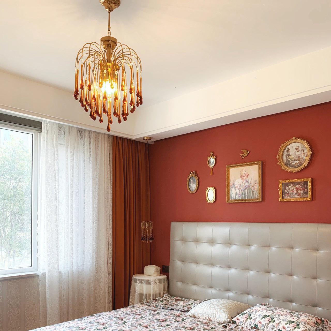 Elegant brass chandelier with amber glass drops hanging in cozy bedroom with red accent wall and floral bedding