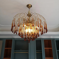 Modern brass chandelier pendant lamp with amber glass teardrop accents hanging in contemporary room